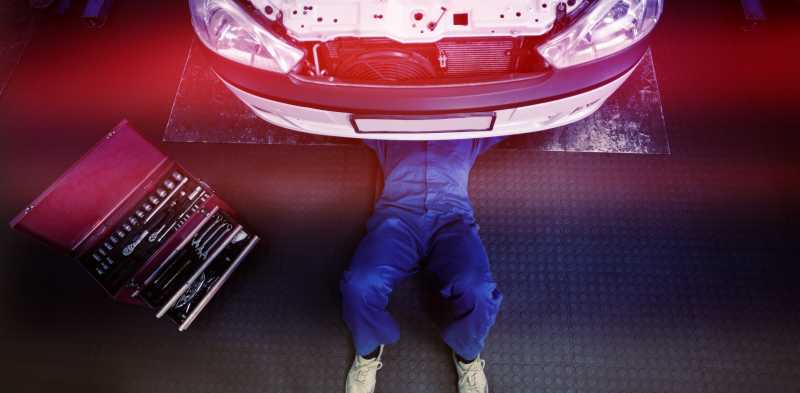 汽车修理厂里一名躺在车下工作的汽车修理工